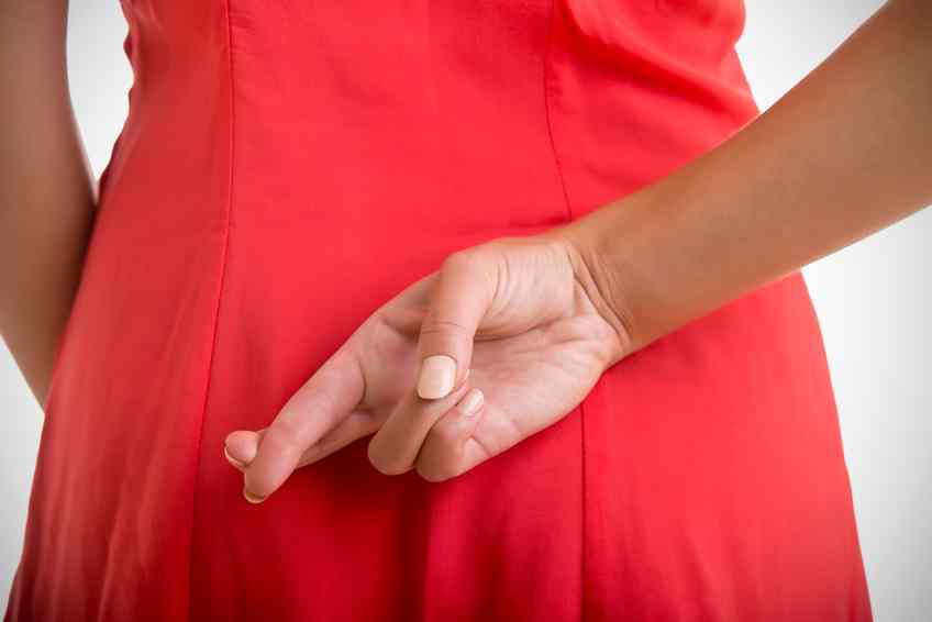 Close up of crossed fingers behind a woman's back